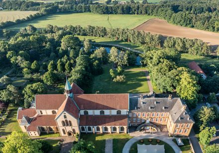 Luftaufnahme eines malerischen Klosters mit roten Dächern, umgeben von Wäldern und Feldern.