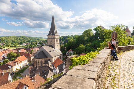 Blick auf Warburg mit mittelalterlicher Kirche, Fachwerkhäusern und grüner Landschaft bei Sonnenschein.