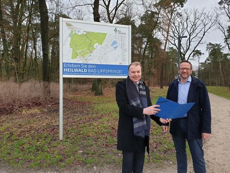 Bürgermeister Ulrich Lange (links) und Sportmediziner Prof. Dr. Dr. Claus Reinsberger vor Schild im Heilwald
