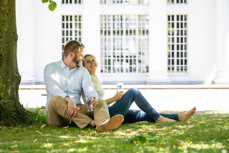 Paar sitzt entspannt auf einer Wiese vor einem großen, weißen Gebäude mit Glasfassade.