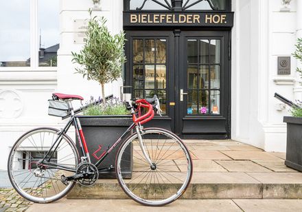 Ein modernes Rennrad steht vor einem eleganten Hoteleingang mit der Aufschrift "Bielefelder Hof".