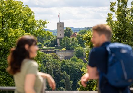 Zwei Menschen betrachten die Sparrenburg im Grünen; im Hintergrund sieht man einen Burgturm.