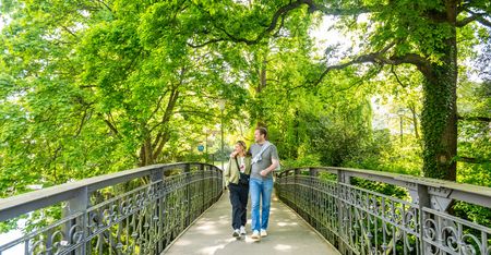 Zwei Menschen spazieren bei sonnigem Wetter über eine Brücke im grünen Aawiesenpark Herford.