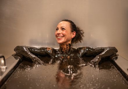 Eine Frau mit braunen Haaren liegt lächeln in der Badewanne mit Moor im Gräflichen Park in Bad Driburg