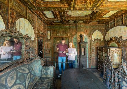 Holzvertäfelter Raum im Junkerhaus mit detaillierten Schnitzereien; zwei Personen betrachten Broschüren.