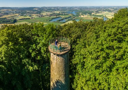 Alter Aussichtsturm im Wald mit Panoramablick auf grüne Felder und blaue Seen in der Ferne.