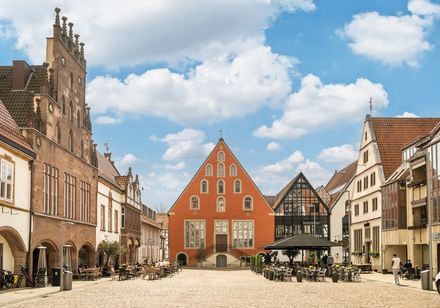 Historische Altstadt mit Kopfsteinpflaster, umgeben von gotischen und modernen Gebäuden unter blauem Himmel.