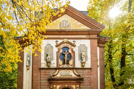 Barockkirche mit verzierten Fassaden, herbstlichen Bäumen und strahlender Sonne im Hintergrund.