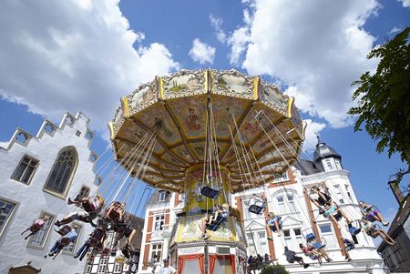 Ein bunter, nostalgischer Kettenkarussell dreht sich vor klassischen Gebäuden unter blauem Himmel.