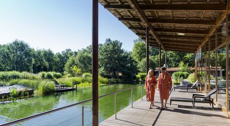 Zwei Personen im Bademantel gehen entlang Teich bei Saunahütte