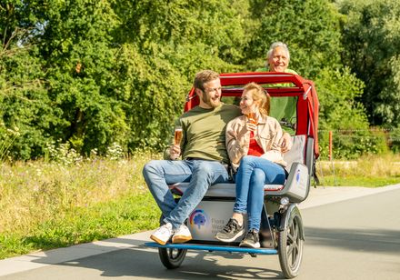 Ein Paar genießt eine gemütliche Rikschafahrt im Flora-Westfalica-Park, während der Fahrer lächelnd das Fahrrad steuert.
