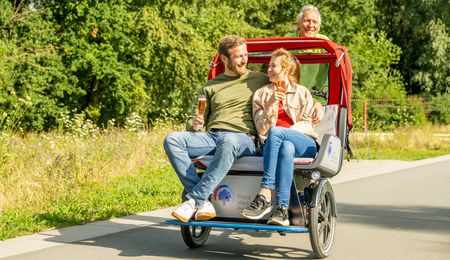 Ein Paar genießt eine gemütliche Rikschafahrt im Flora-Westfalica-Park, während der Fahrer lächelnd das Fahrrad steuert.