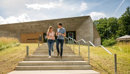 Ein Paar spaziert eine moderne Treppe hinunter, vor einem futuristisch gestalteten Gebäude.