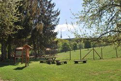 Ein weitläufiges Wildgehege mit Holzbänken, Informationstafeln, grünem Gras und Bäumen im Vordergrund.