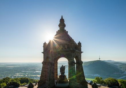 Monument auf einem Hügel mit Statue in der Mitte, umgeben von strahlendem Sonnenlicht.