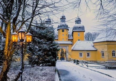 Gelbes Jagdschloss Holte im Schnee, vorne eine Laterne