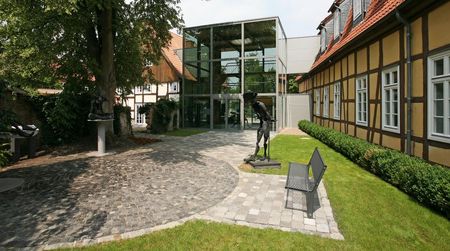 Moderne Glasfassade verbindet historische Fachwerkgebäude in gepflegter Parklandschaft.