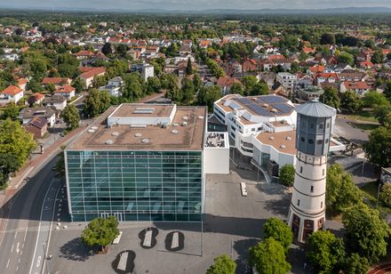 Luftaufnahme eines modernen Gebäudekomplexes mit Glasfassade und angrenzendem historischen Turm.