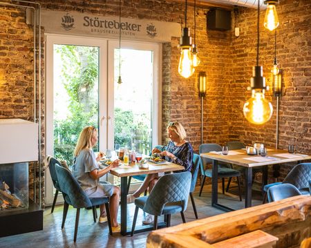 Zwei Frauen speisen in einem gemütlichen Restaurant mit Backsteinwänden und modernen Lampen.
