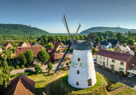 Alte Windmühle in Porta Westfalica, umgeben von grünen Hügeln und Wohnhäusern bei klarem Himmel.