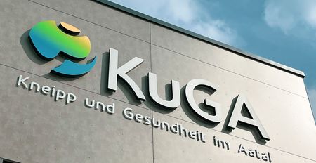 Fassade des Gesundheitszentrums KuGA mit modernem Logo und Schriftzug unter blauem Himmel.