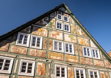 Historisches Fachwerkhaus mit prachtvollen Fresken und vielen Fenstern, blauer Himmel im Hintergrund.