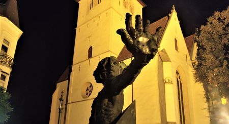 Eine imposante Skulptur vor einer beleuchteten, gotischen Kirche bei Nacht, Herford.