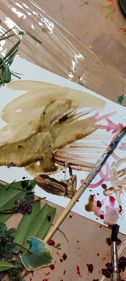 Künstlerische Materialien und natürliche Elemente wie Blätter und Pigmente auf einem Arbeitstisch verteilt.