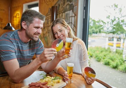 Ein Paar genießt Bierproben in einer Brauerei, umgeben von warmem Holzinterieur und Tageslicht.
