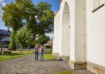 Ein Paar spaziert auf einem gepflasterten Weg neben einem weißen Gebäude und einem großen Baum.