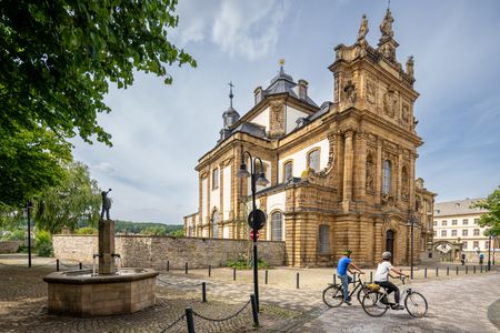 Barocke Kirche aus gelbem Sandstein mit aufwendigen Verzierungen, umgeben von Fahrradfahrern.