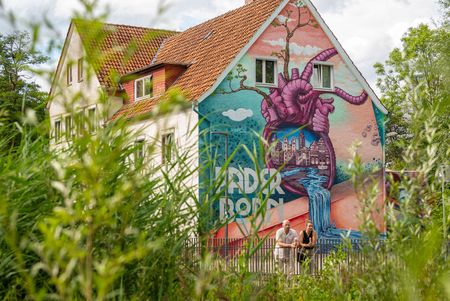 Zwei Personen vor Herzgraffiti in Paderborn, vorne Sträucher