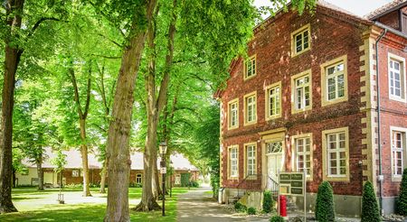 Backsteingebäude im Grünen mit Bäumen davor, nahe Kirchplatz Clarholz im Teutoburger Wald.