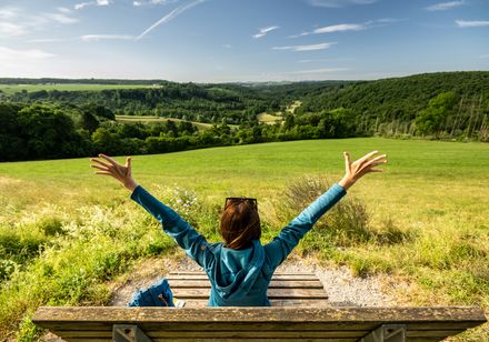 Frau sitzt auf Liege in der Natur und streckt Arme aus