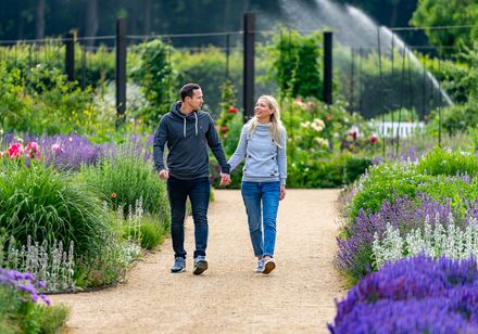 Ein lachendes Paar spaziert auf einem Kiesweg durch einen bunt blühenden, gepflegten Garten.
