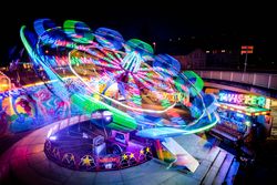 Leuchtendes Karussell vor nächtlicher Kulisse, umgeben von bunten Ständen und Lichtern.
