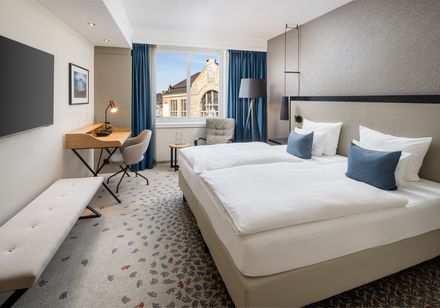 Modern gestaltetes Hotelzimmer mit Doppelbett, das Aussicht auf ein historisches Gebäude bietet.