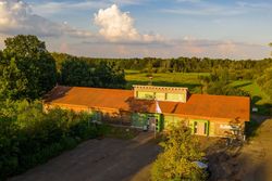 Ein niedriges Gebäude mit rotem Dach vor grüner Landschaft und blauem Himmel mit Wolken.