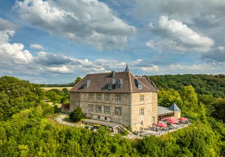 Luftaufnahme Burg Schwalenberg mit bewaldetem Hintergrund unter malerisch bewölktem Himmel.
