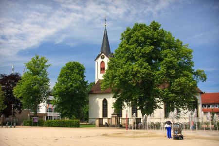 Marktplatz Leopoldshöhe mit Springbrunnen, Kirche und Bäumen; Familie mit Kinderwagen im Vordergrund.