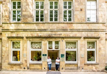 Historisches Gebäude aus Sandstein mit Aufschrift Stahlbadehaus, zwei Personen am Eingangsportal.