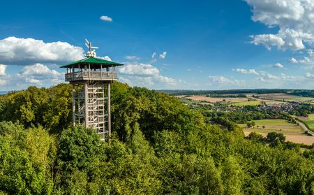 Aussichtsturm in Marienmünster auf bewaldetem Hügel, mit weitem Blick über ländliche Felder und Dörfer unter blauem Himmel.
