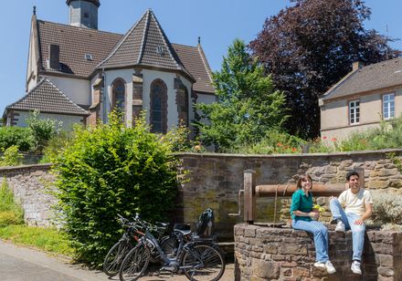 Zwei Personen sitzen auf einer Brunnengeländemauer vor einer historischen Kirche in Marienmünster. Fahrräder stehen daneben.