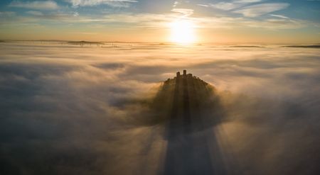 <p>Ruine Fertőrákos bei Sonnenaufgang, umgeben von dichtem Wolkenmeer, Sonnenstrahlen strahlen hervor.</p>