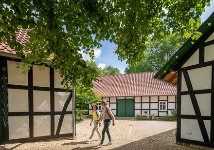 Zwei Menschen spazieren durch einen gepflasterten Hof, umgeben von traditionellen Fachwerkhäusern.