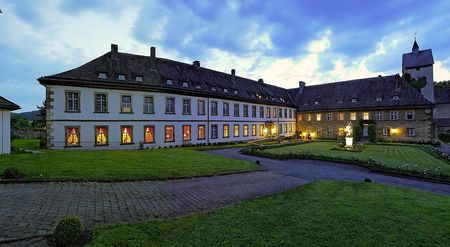 Beleuchtetes Schloss Gehrden bei Dämmerung, umgeben von gepflegtem Rasen und wolkigem Himmel.