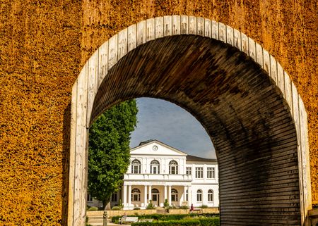Historisches, weißes Empfangsgebäude im Kurpark Bad Hall, eingerahmt von einem Salinenbogen.