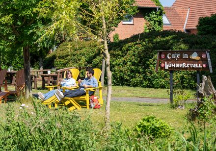 Zwei Personen entspannen sich in gelben Liegestühlen im Garten eines Cafés namens "Hühnerstall".