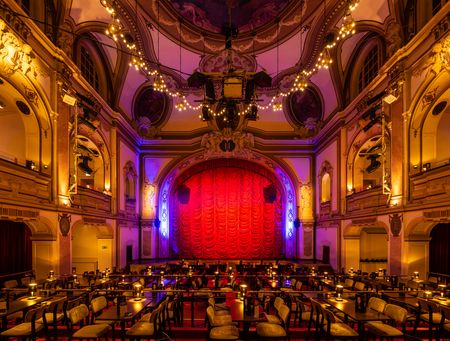Ein prächtig illuminierter Theaterraum mit verzierten Wänden und einer roten Bühnencurtain.