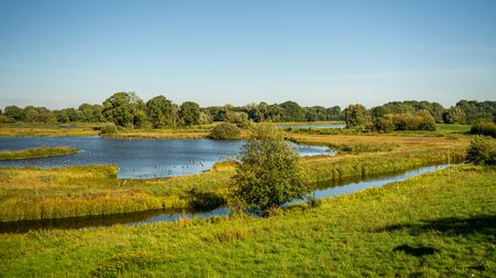 Weite grüne Landschaft mit Flusslauf und Wasserflächen bei strahlend blauem Himmel in Delbrück.